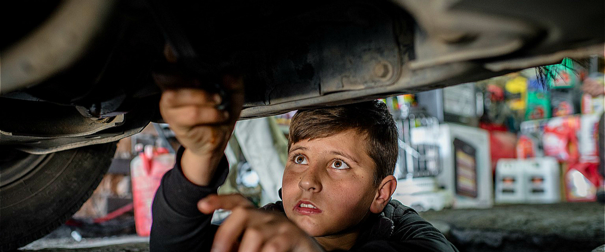 محمد (14 عامًا)، لاجئ سوري من مدينة عين العرب في حلب، يعمل تحت سيارة في ورشة لإصلاح السيارات في أربيل، العراق في أذار/مارس 2016. وتظهر دراسة لمنظمة العمل الدولية أن هناك علاقة قوية بين عمالة الأطفال وحالات الصراع والكوارث. يونيسف/ UN020145
